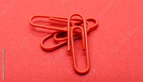 Red Paperclips Close-Up on Red Surface. Close-up view of several red paperclips overlapping on a red textured background.