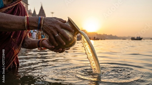 Woman pouring water from a traditional brass vessel into a river during sunrise