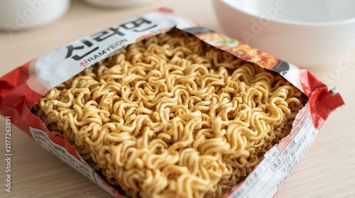 Uncooked dried instant noodle block in open packaging on a wooden table