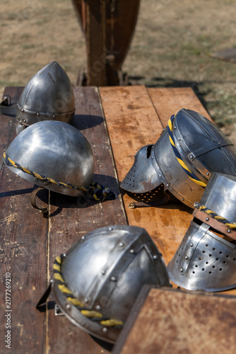 фотографія Medieval knight steel helmets displayed on a wooden table during an outdoor historical reenactment
