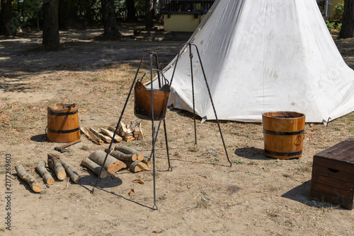 Canvastavla Medieval campsite setup with a tripod cauldron, wooden buckets, firewood, and a canvas tent outdoors