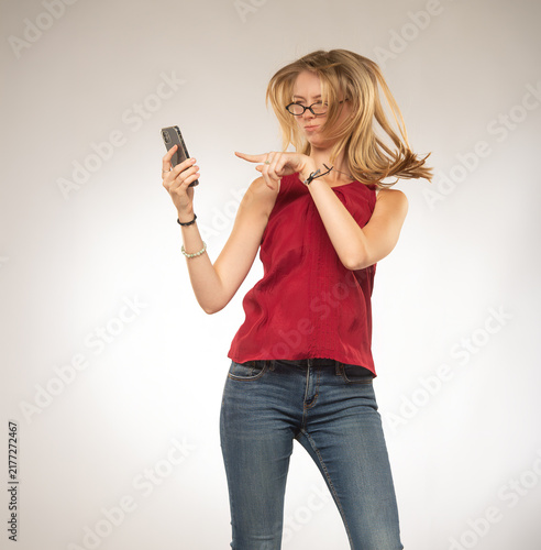 young woman in a red blouse and blue jeans with flowing hair holding a smartphone in her hand on a white background with free space for text