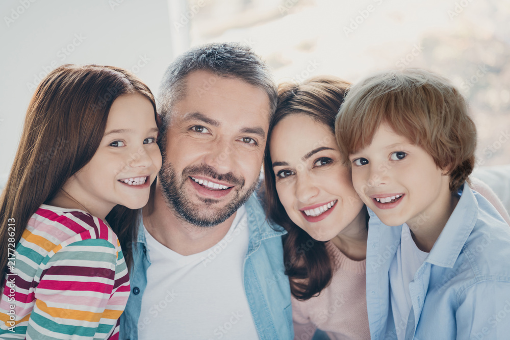 Fototapeta premium Happy family portrait of parents and two children smiling together at home, casual joyful family moment showing love, bonding and togetherness in a bright cozy living room