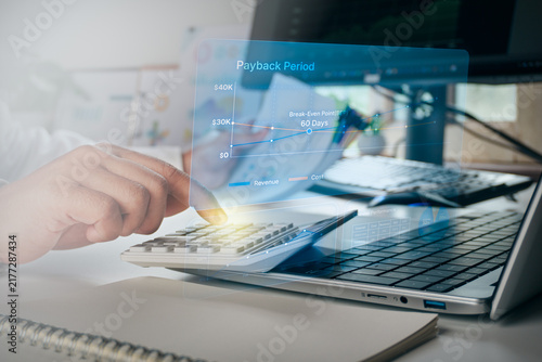 Photography Business professional using calculator with digital hologram interface of payback period and break-even point financial graph, concept of business ROI, investment analysis, and financial planning