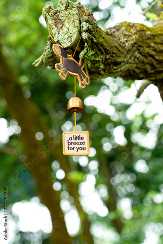 Foto Cute Wind Chime with Small Brass Bell and Dog Figure Hanging on Tree Branch in O