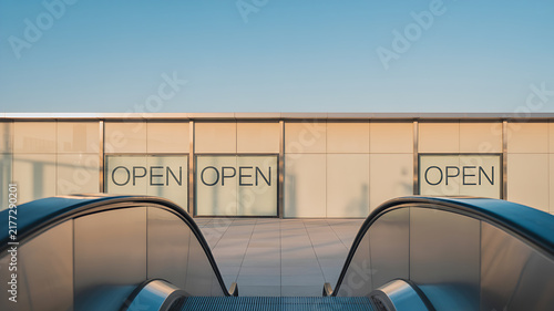 Outdoor escalator leading up to modern building entrance with open signs on glass under clear blue