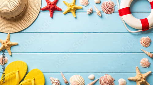 Summer vacation background with straw hat flip flops and seashells on a blue wooden surface