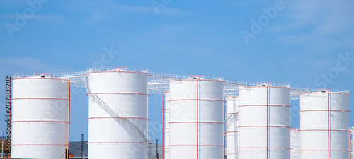 Foto Large white oil storage tanks in fuel refinery plant with clear blue sky background