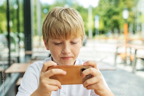 Fotografie Preteen boy playing mobile video game on smartphone outdoors