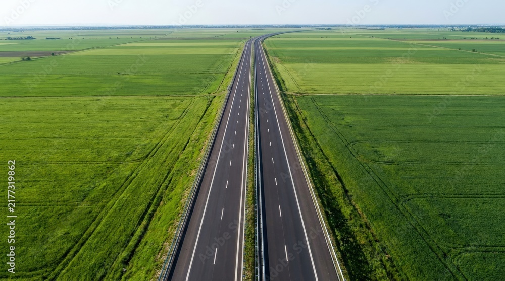 Obraz premium Aerial top view of a modern asphalt highway through lush green fields