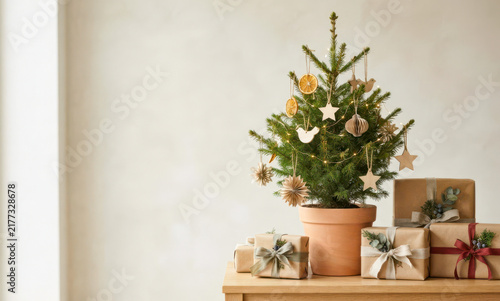 Potted fir tree standing on a wooden surface with sustainable christmas decorations and wrapped presents