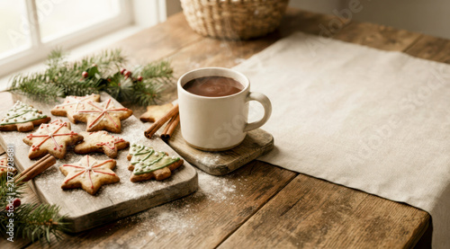 Christmas sweet tree cookies, hot cocoa, and cinnamon sticks decorating a rustic wooden table for holidays.