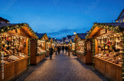 Christmas market stalls line a cobblestone street, selling festive decorations and treats under evening lights. Ai generated