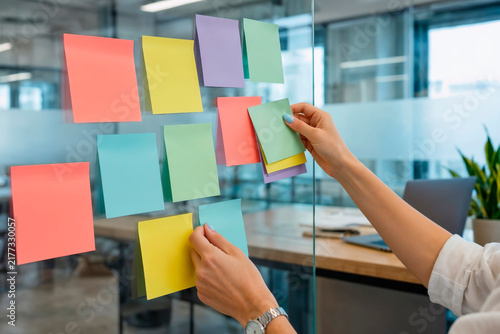 Hands Placing Colorful Sticky Notes on Glass Wall During Planning Session