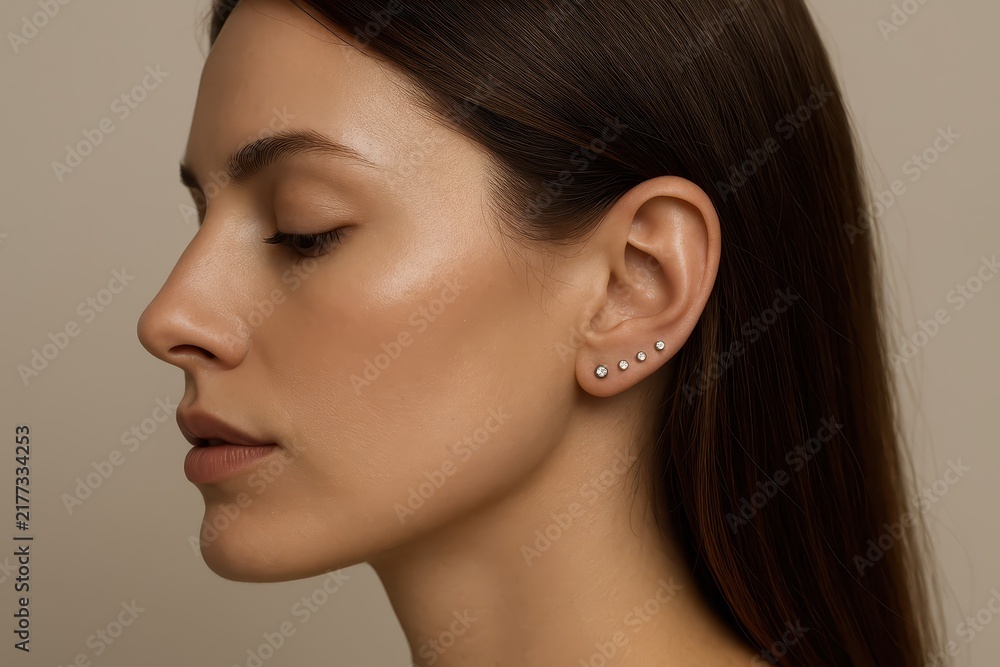 Fototapeta premium Profile of woman with multiple earrings against neutral background