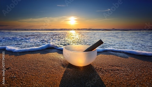 White Crystal Singing Bowl On A Sandy Beach At Sunset With Ocean Waves