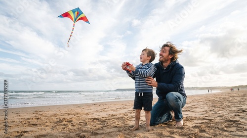 Father and son flying a colorful kite on a sandy beach