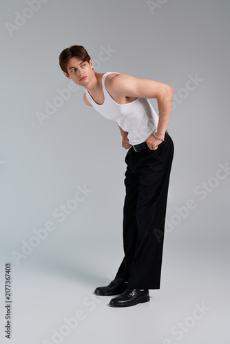 Canvas Print A stylish young man poses confidently in a tank top and trousers against grey