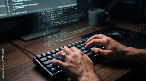 Software developer coding on mechanical keyboard with computer programming code on monitor