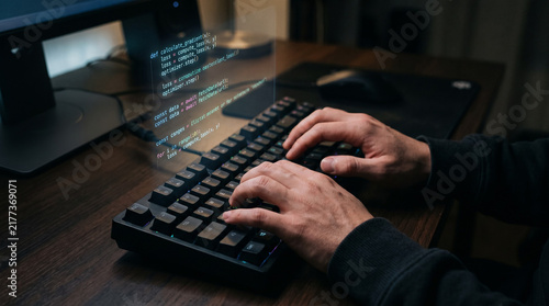 Software developer coding on mechanical keyboard with computer programming code on monitor