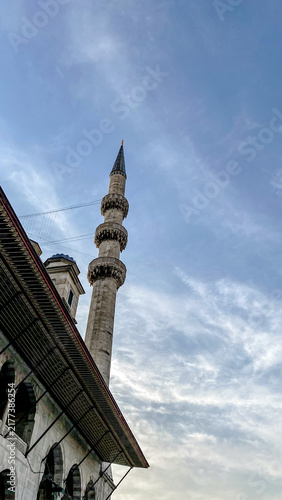 Obraz na płótnie New Mosque Yeni Cami minaret rising above ornate roofline under cloudy sky in Is
