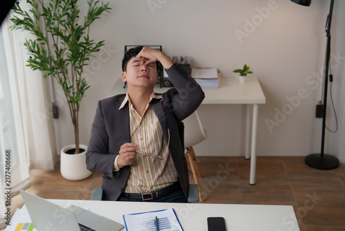 Canvastavla Asian businessman rubbing temples and holding glasses, experiencing intense head