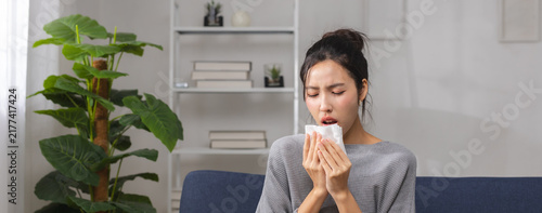Fotografía woman sneezing into tissue while feeling sick at home, showing respiratory symptoms and illness