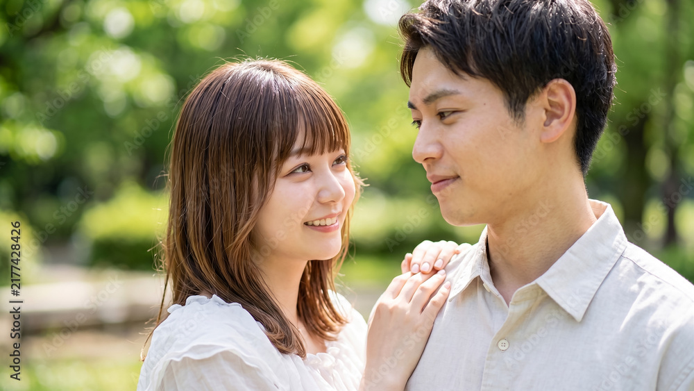 Fototapeta premium Happy young couple in love looking at each other outdoors in a park, romantic relationship concept