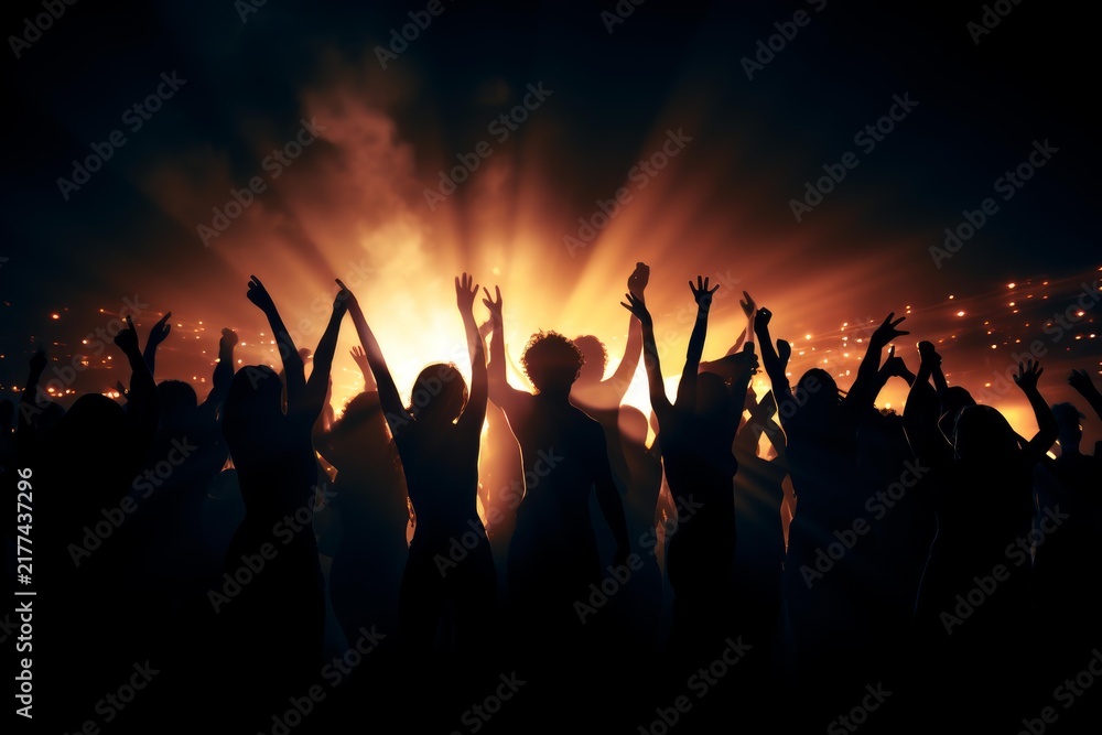 Fototapeta premium Audience cheering and partying with arms raised in silhouette against bright stage lights