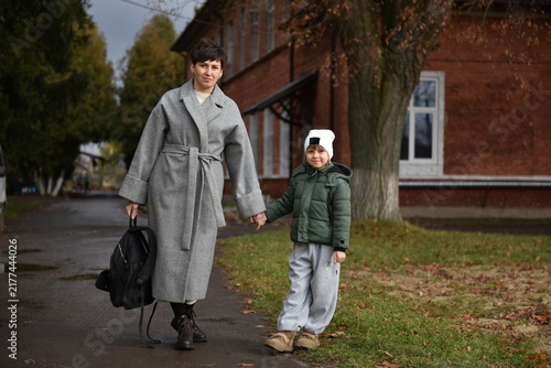 Mother and little daughter holding hands while walking outdoors in autumn. Woman with a backpack and child in warm clothes