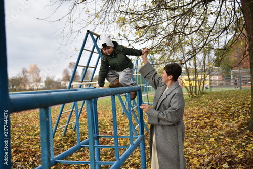 Mother assisting daughter on a blue metal playground structure in autumn