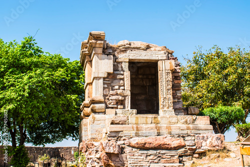 Photography Broken stone temple ruins at Chittorgarh Fort, surrounded by lush green trees an