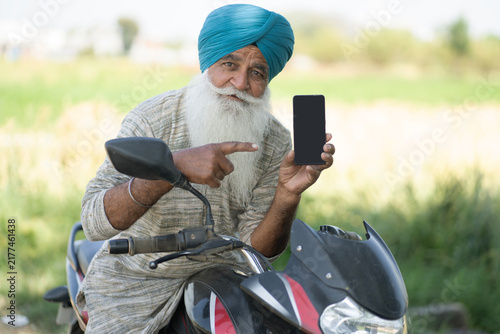 Bild auf Leinwand Indian punjabi sikh farmer showing mobile phone  screen while sitting on motorbi