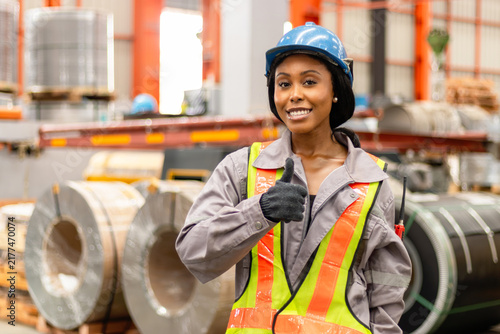 Принти на полотні Portrait of happy young African American worker with helmet in safety clothing giving thump up in manufacturing factory