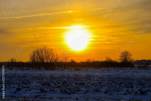 Konstfotografi A bright winter sun sets over a snow-covered field