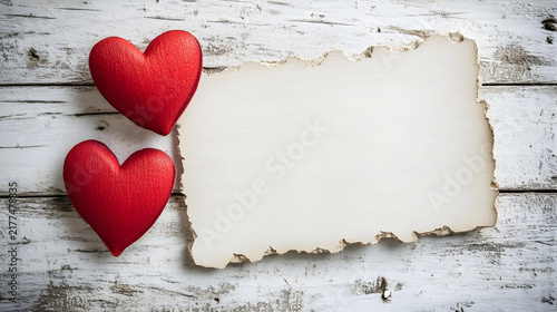 Two red hearts beside a blank torn note on a weathered wooden surface with aged wooden background rests beside arrangement decorative minimalist affection sentiment with plainness