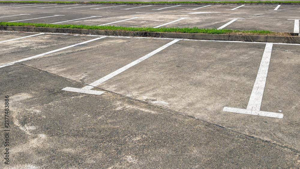 Obraz premium Empty parking lot on a clear day, asphalt ground with bright white parking lines, featuring a curb and green grass border, representing urban infrastructure and available space