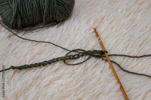 Wooden crochet hook inserted into a row of green wool yarn stitches resting on a white fluffy fur background close-up. Crocheting project, handmade yarn craft, needlework process, and cozy hobby conce