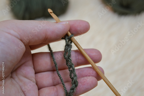 Canvas Print Woman hand holding a wooden crochet hook working on a green wool yarn chain close-up