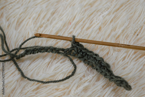 Wooden crochet hook inserted into a row of green wool yarn stitches resting on a white fluffy fur background close-up. Crocheting project, handmade yarn craft, needlework process, and cozy hobby conce