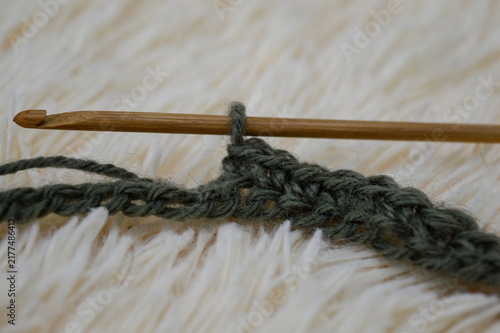 Wooden crochet hook inserted into a row of green wool yarn stitches resting on a white fluffy fur background close-up. Crocheting project, handmade yarn craft, needlework process, and cozy hobby conce