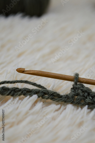 Wooden crochet hook inserted into a row of green wool yarn stitches resting on a white fluffy fur background close-up. Crocheting project, handmade yarn craft, needlework process, and cozy hobby conce