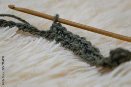 Konstfotografi Wooden crochet hook inserted into a row of green wool yarn stitches resting on a white fluffy fur background close-up