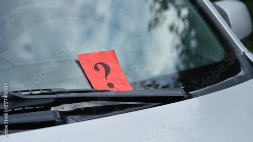 Photography A crumpled red paper note with a black question mark is placed under a windshield wiper of a car, representing a mystery message or an unexpected notification