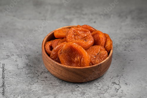 Sweet orange dried apricots kuraga in small round wooden bowl on gray textured stone background close up side view
