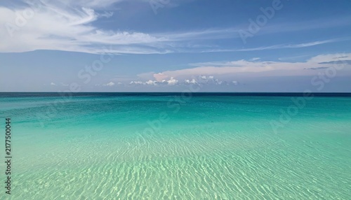 Crystal clear turquoise tropical ocean water under a bright blue sky with light clouds.