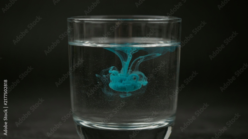 Obraz premium A clear glass filled with water showing blue ink spreading across the center.