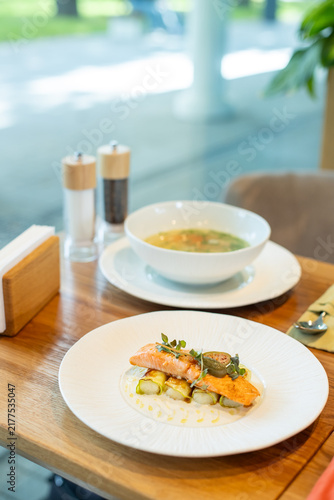 Konstfotografi Salmon and zucchini roll on a plate with a bowl of soup and salt and pepper shakers on a wooden table