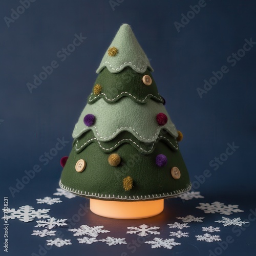 A small handmade felt christmas tree with colorful decorations and glowing wooden base on dark surface