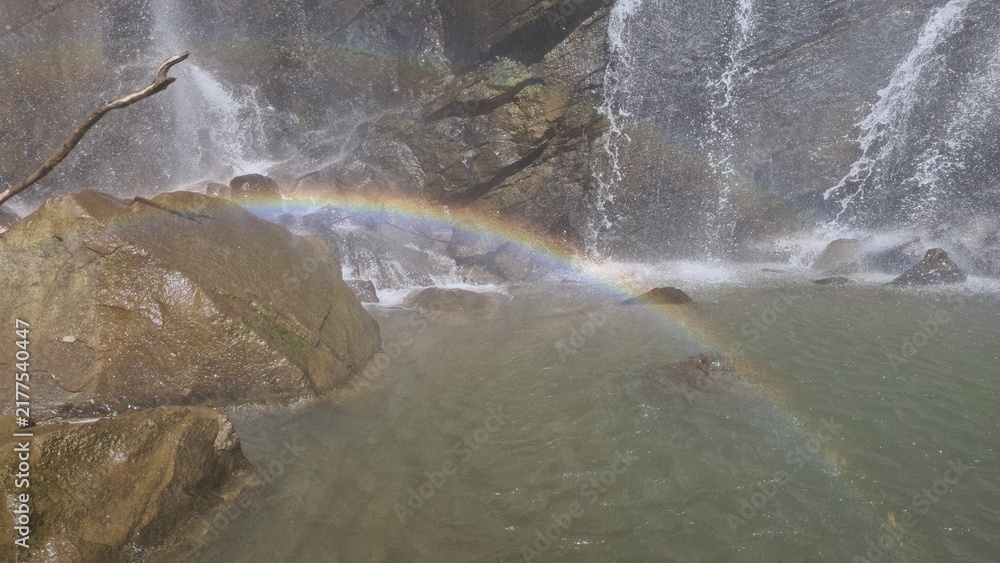 Obraz premium A vibrant rainbow arcs over the tranquil, mist-kissed waters of a cascading waterfall, showcasing nature's breathtaking beauty